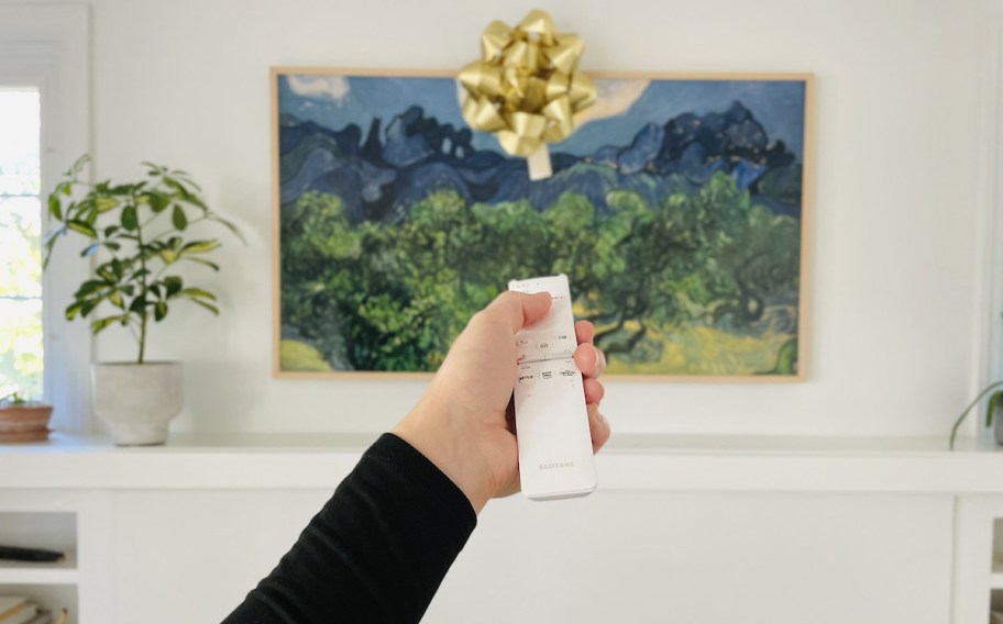 hand holding white remote control with picture frame tv in background with gold bow