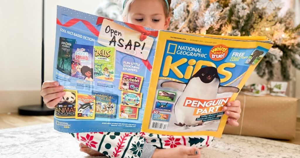 girl holding an open national geographic kids magazine in front of a christmas tree