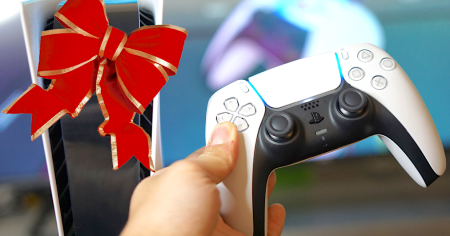 PS5 controller in hand next to a console with a red and gold holiday bow on it