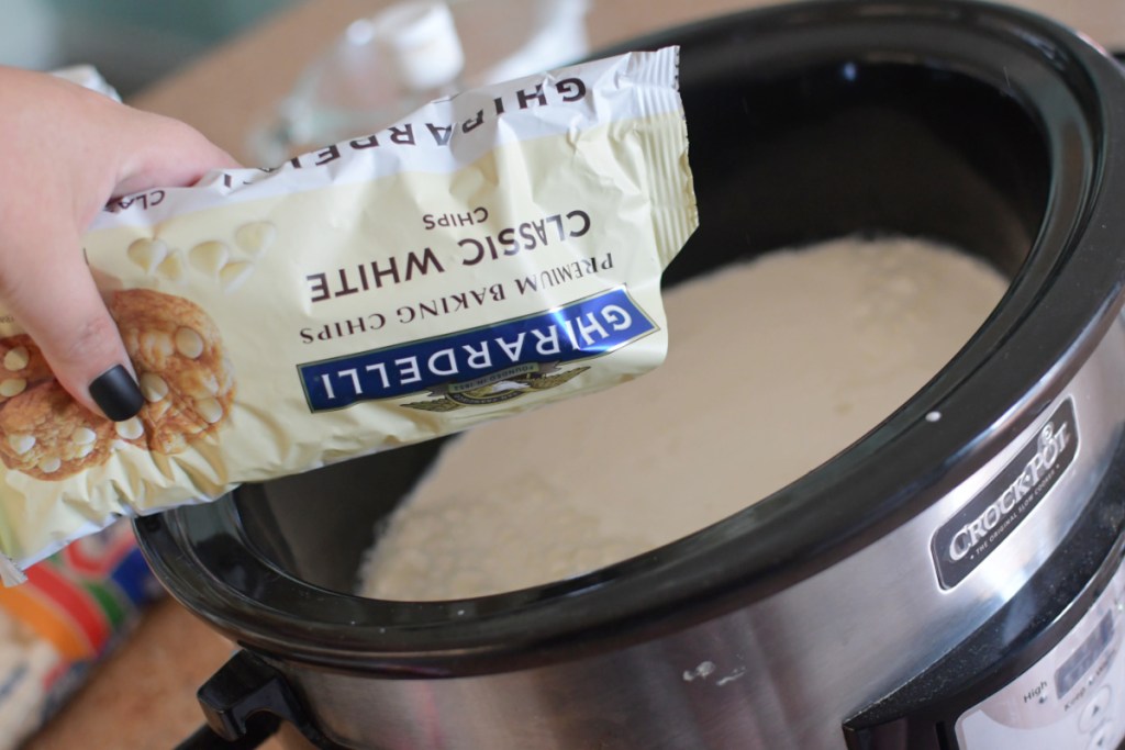 Pouring white chocolate chips into a slow cooker for grinch hot chocolate