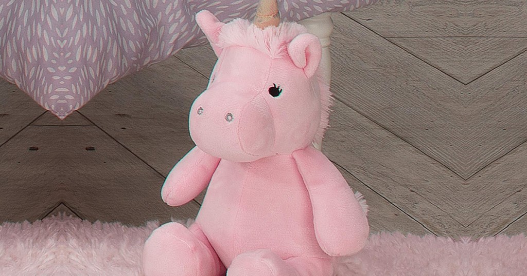 pink plush unicorn sitting on a floor near a bed