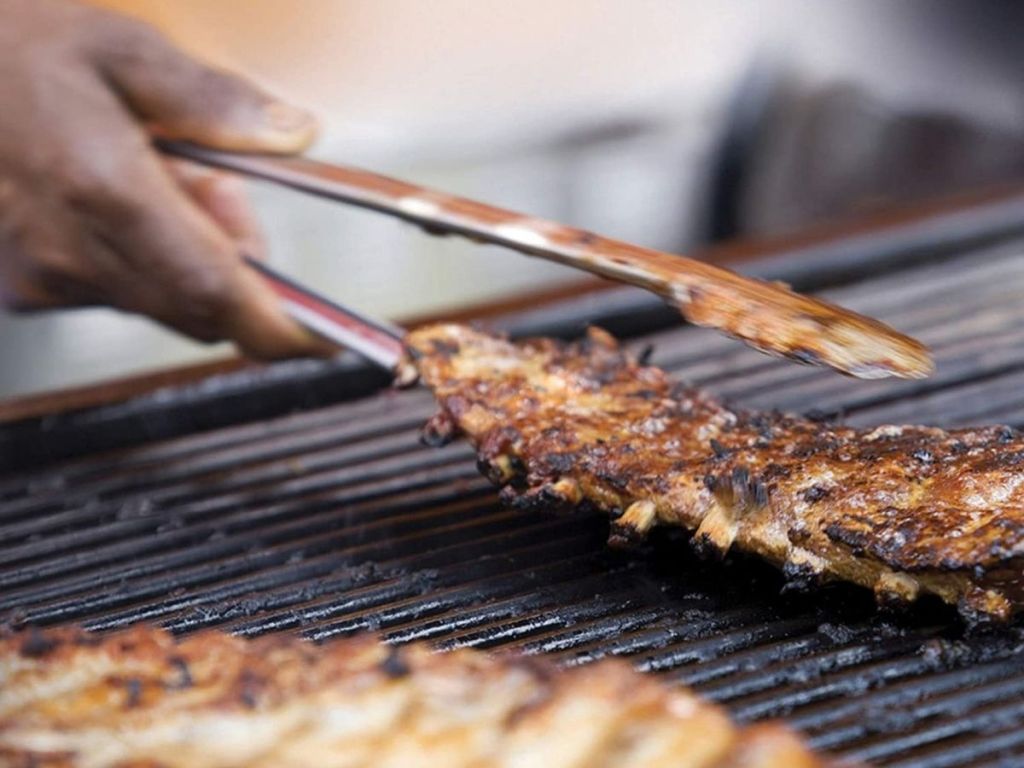 person using tongs to flip ribs