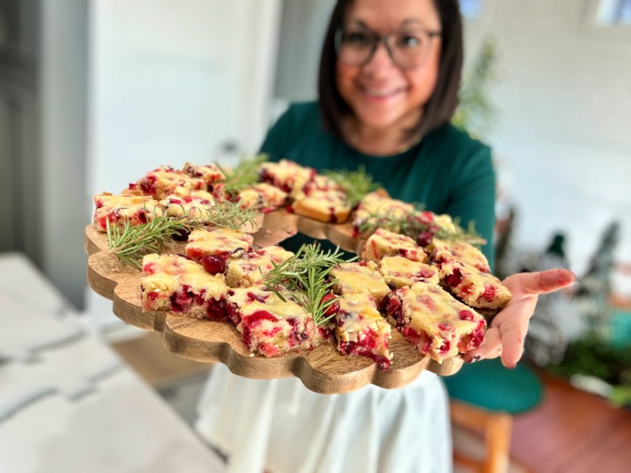 woman holding a wood tray with cranberry christmas bars 