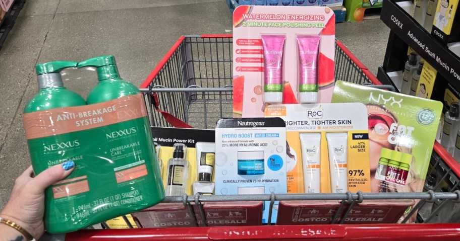 Costco shopping cart with Neutrogena, NYX, COSRX and ROC beauty items in it, hand next to it holding a Nexxus shampoo and conditioner est