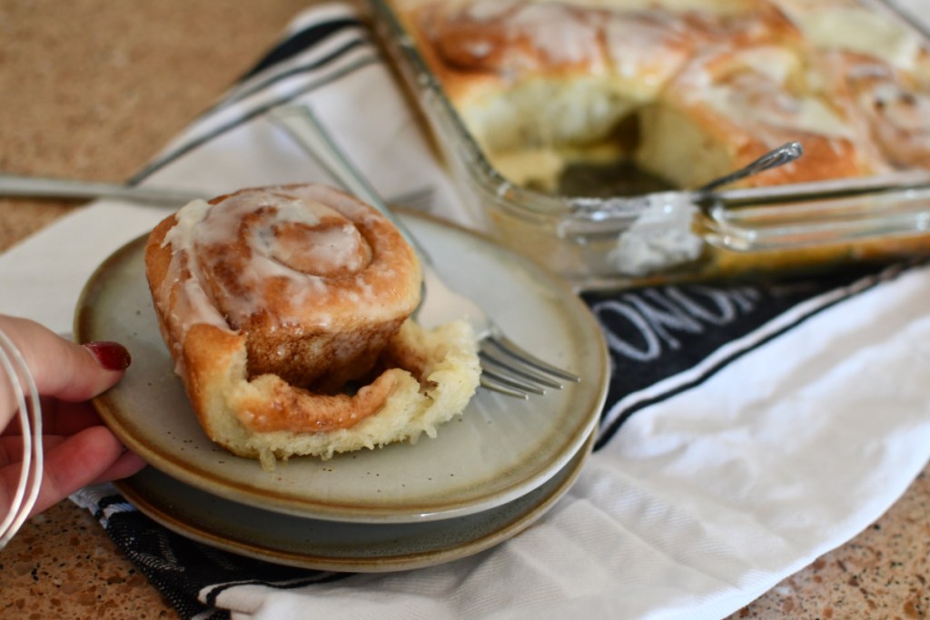 hand holding a plate containing rhodes cinnamon rolls with whipped cream 