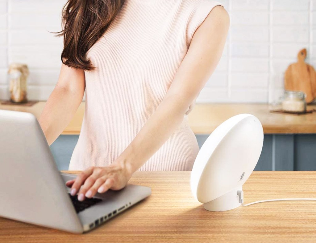 woman on laptop near light therapy lamp