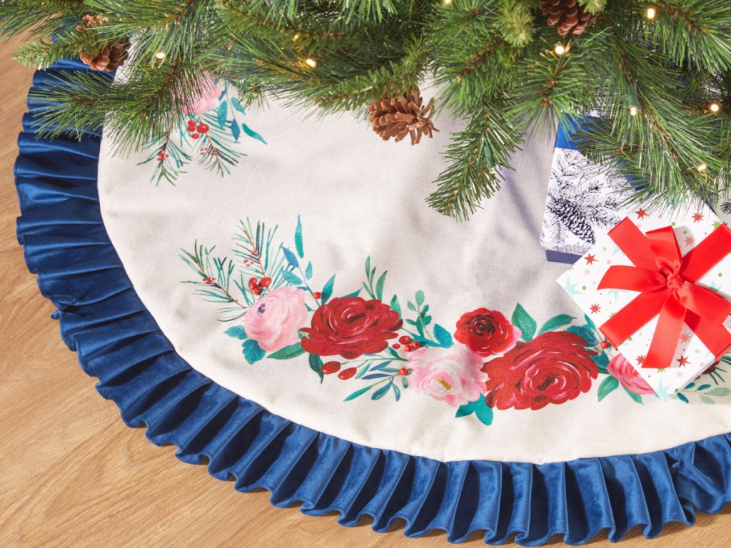 The Pioneer Woman Blue Ruffle & Red Roses Christmas Tree Skirt displayed on the floor with gifts around it