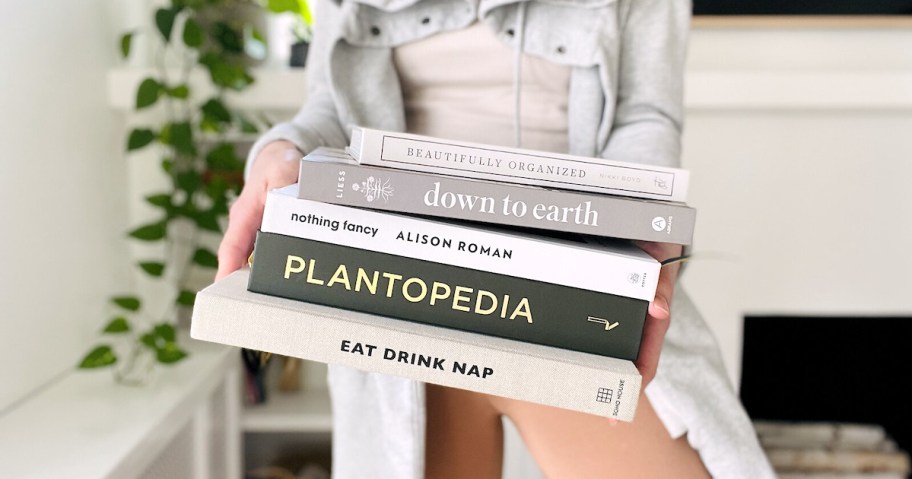 woman holding stack of coffee table books