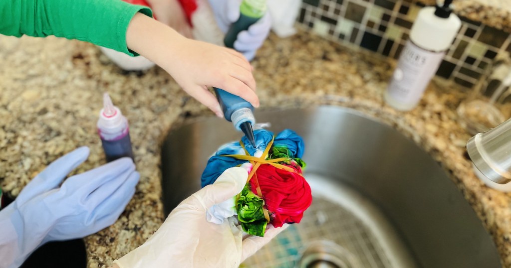 hands squirting tie dye on balled up shirt over sink