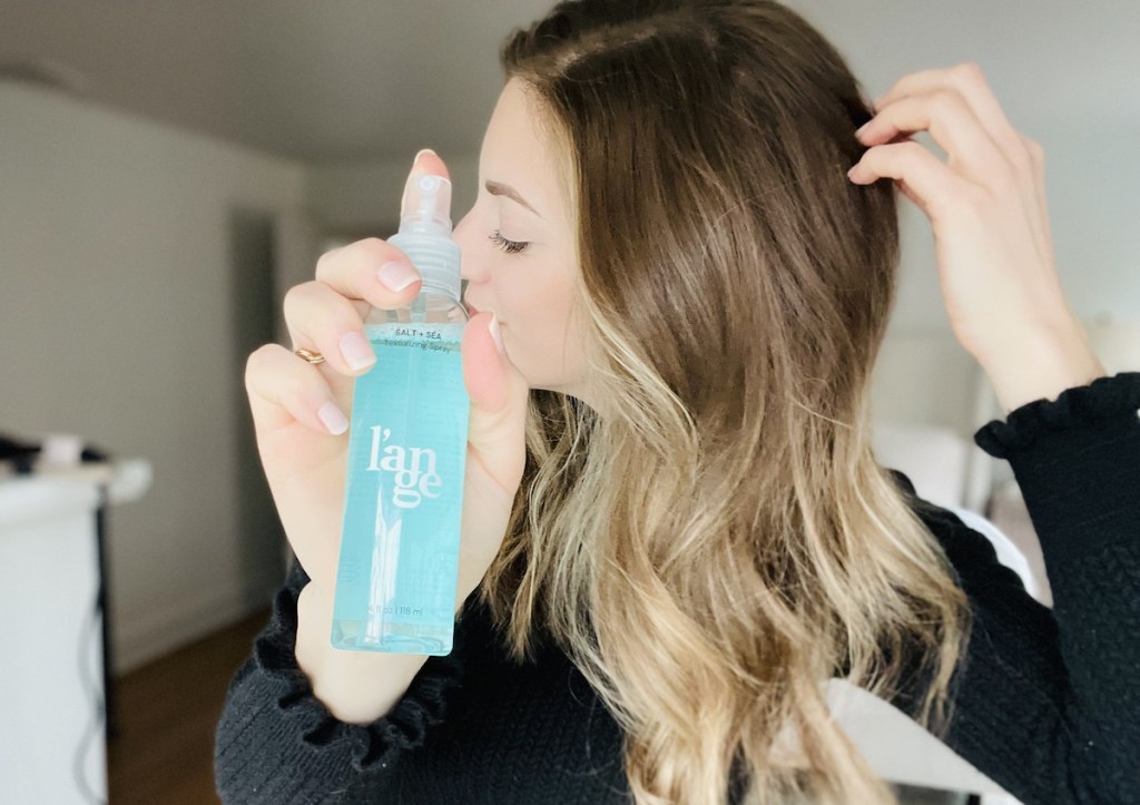 woman holding bottle of blue salt sea spray in hand touching hair