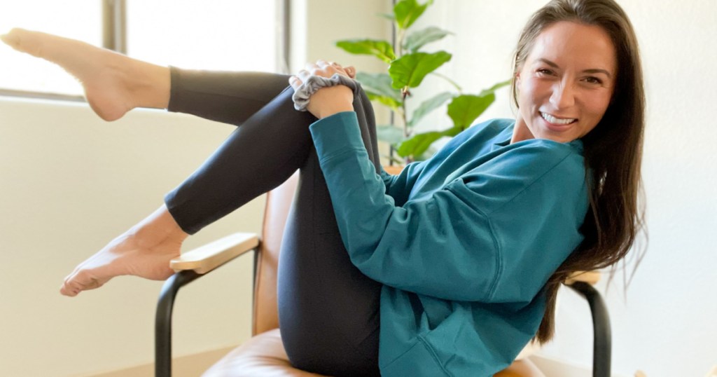 woman smiling and sitting in chair wearing a teal green Marika shirt and black leggings