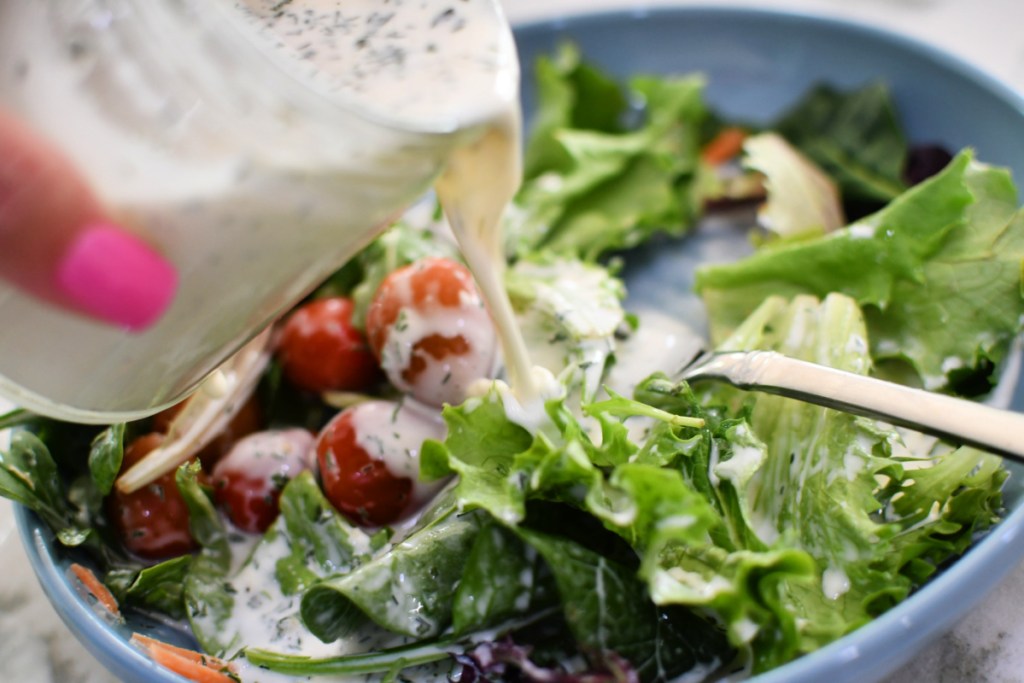 pouring ranch dressing on a salad