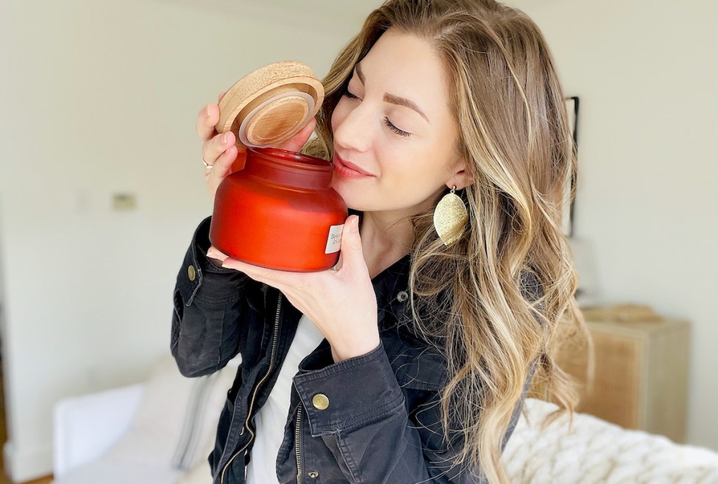 woman holding red candle and wood lid with eyes closing smelling volcano candle dupe