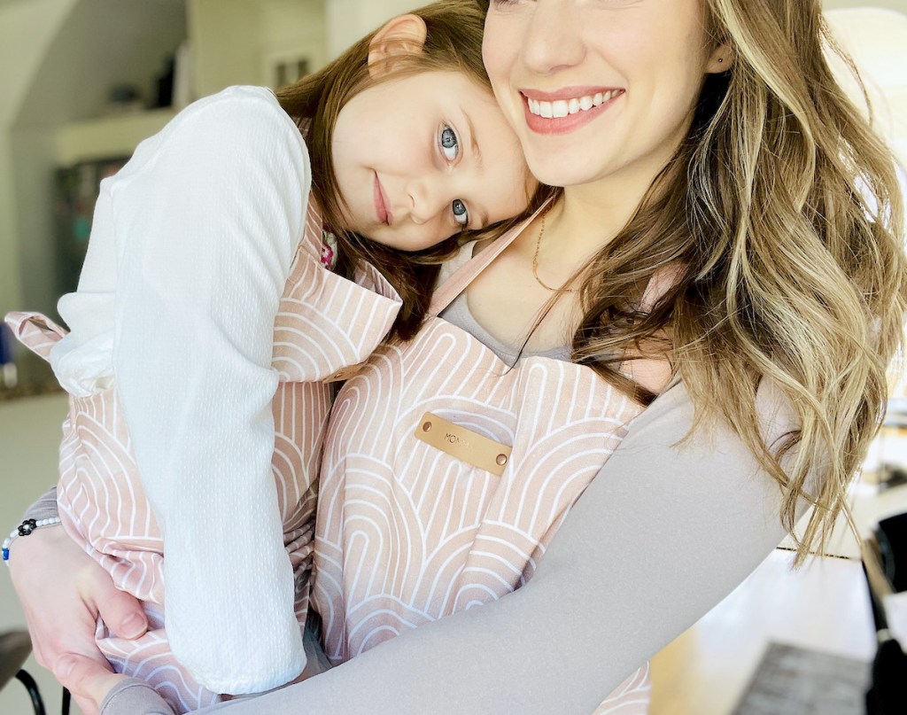 mom holding little girl wearing matching pink and white apron