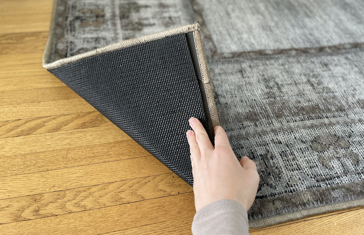 hand holding up corner of rug on wooden floor