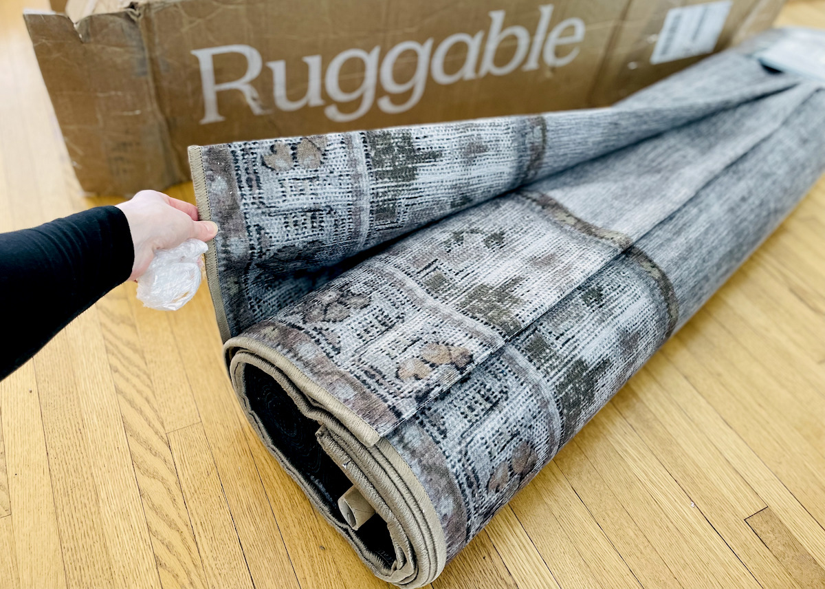 hand holding edge of rolled vintage rug laying on wood floor