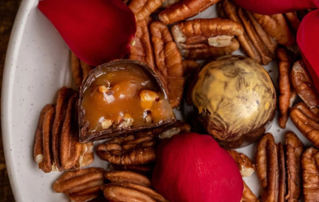 chocolate nut and caramel truffle cut in half sitting on plate with rose petals and pecans