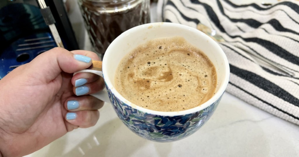 holding a frothy americano coffee