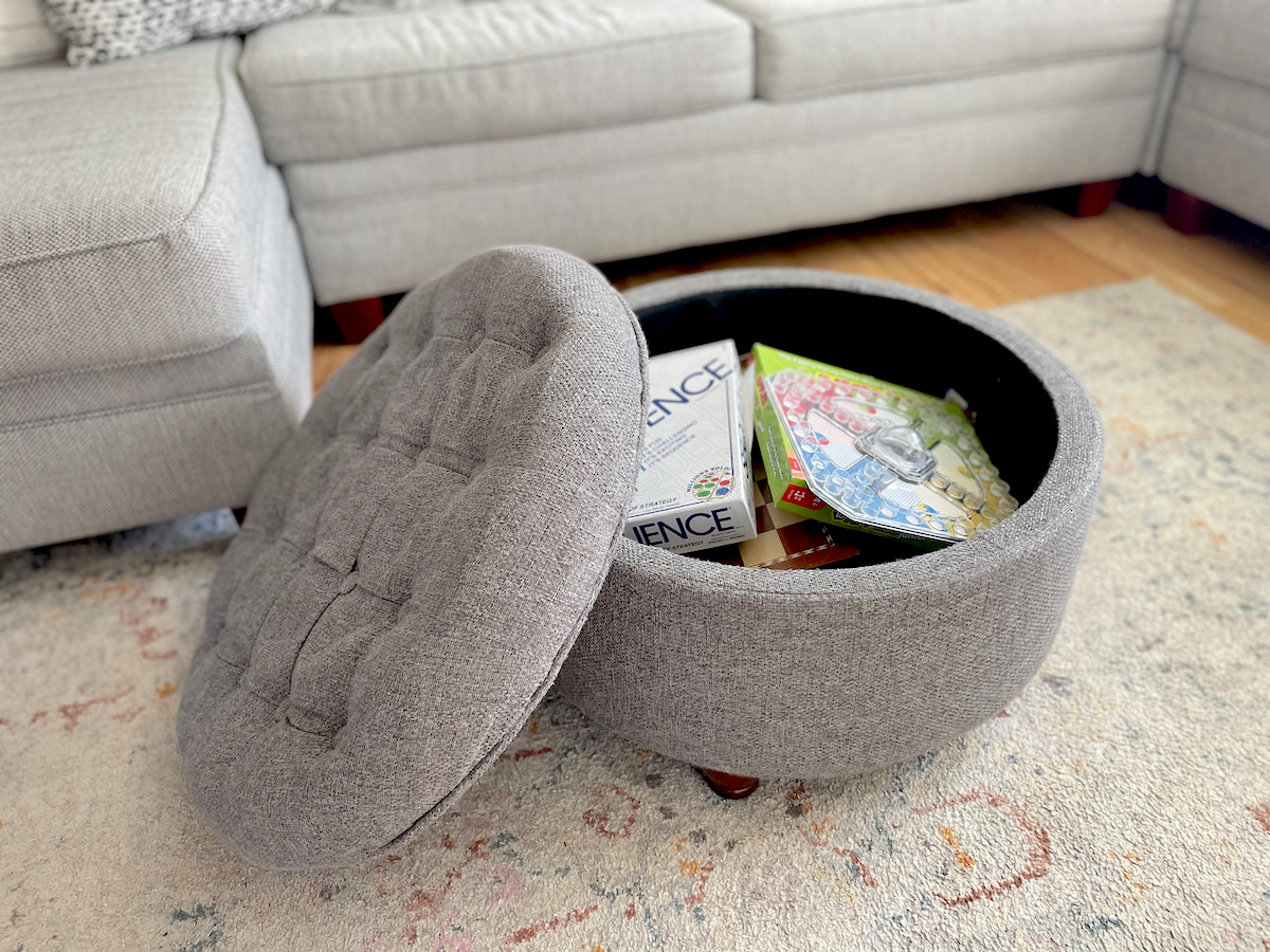 gray tufted storage ottoman on floor with board games inside