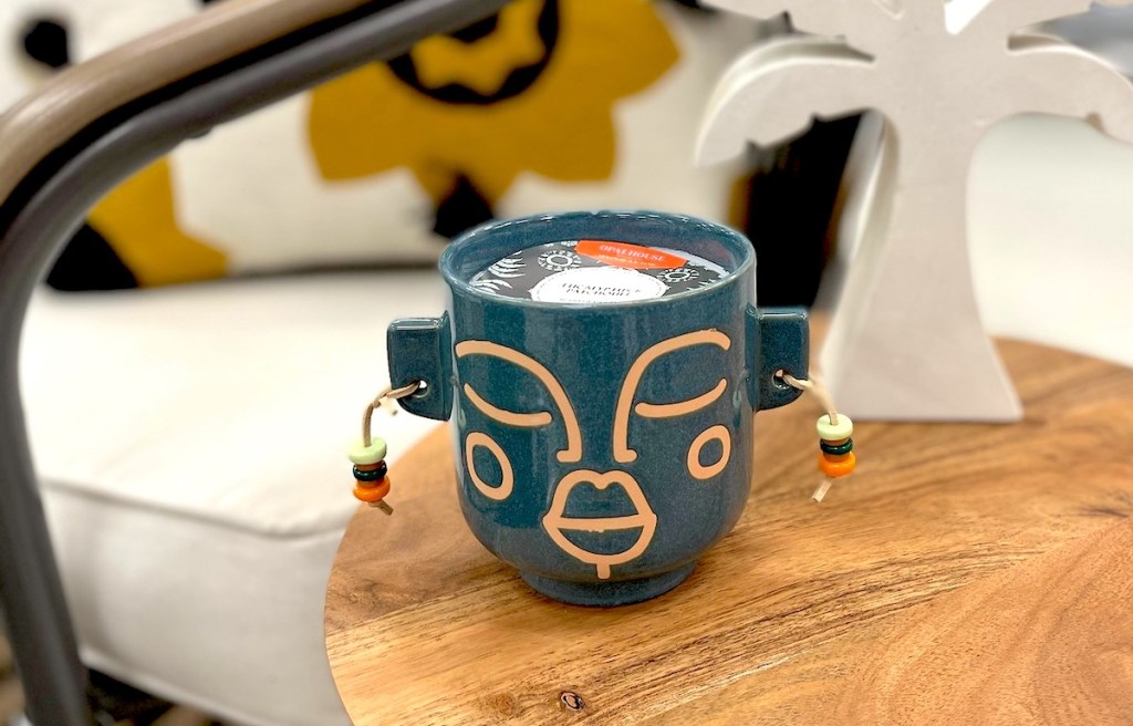 blue candle with face and earrings sitting on wood table