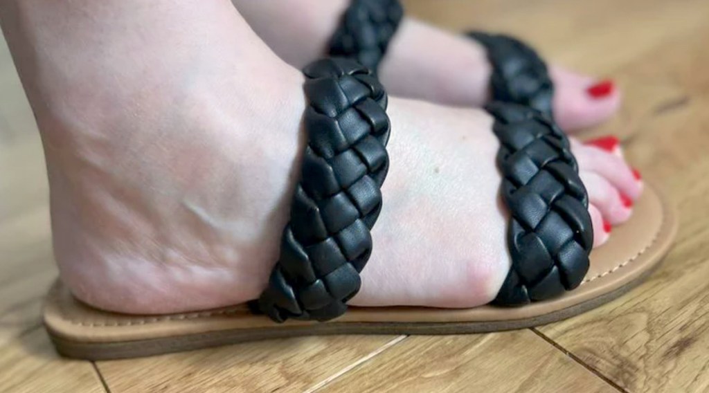 close up of feet wearing black braided sandals on wood floor