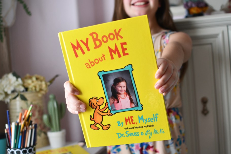 girl holding a book up to the camera with the title "My Book about Me"