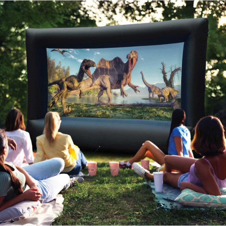 family watching dinosaur movie on outdoor screen in yard