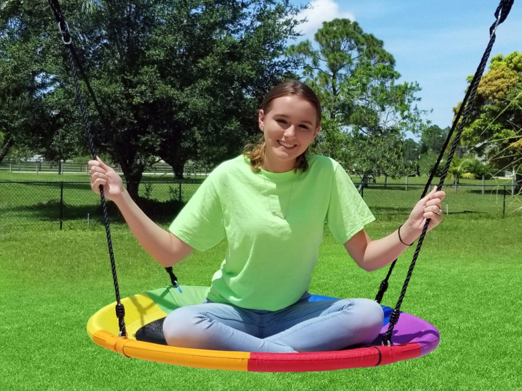 girl sitting in rainbow saucer swing outside