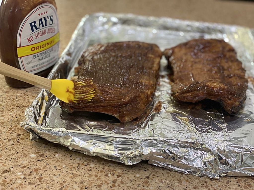 person coating spare ribs with bbq sauce