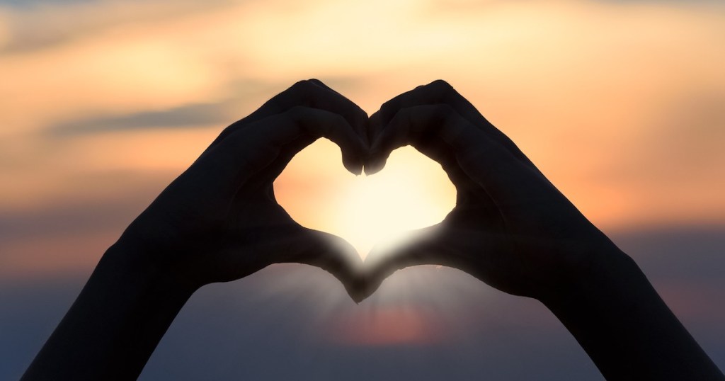 hands in the shape of a heart in front of sunset