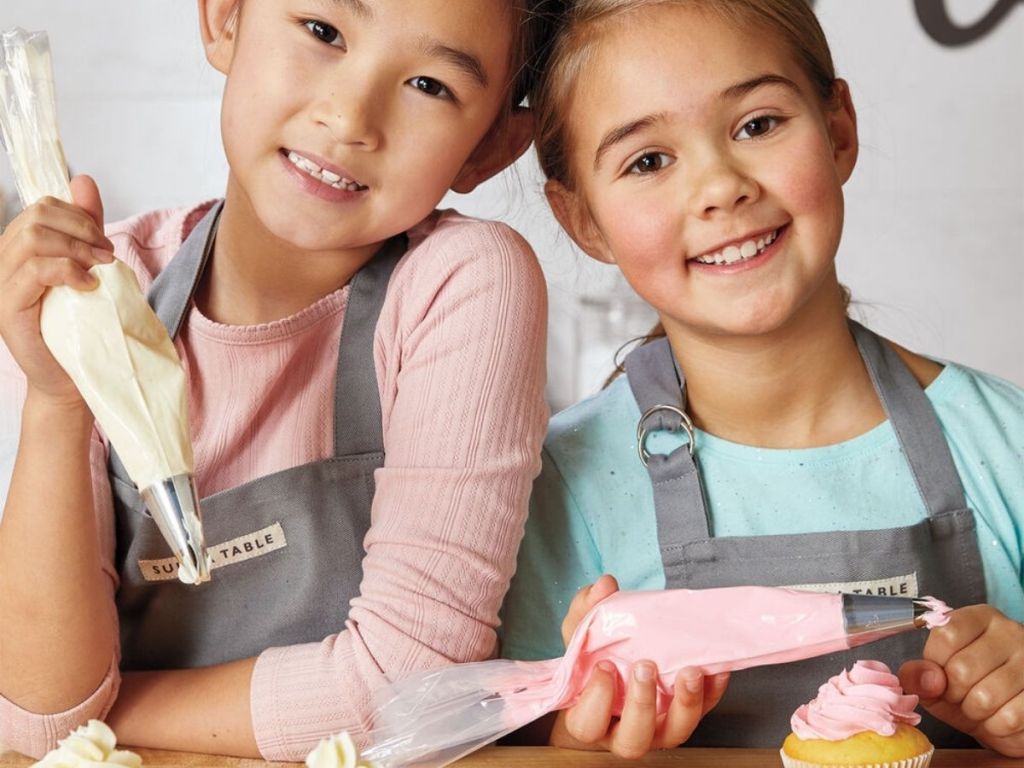 2 girls wearing aprons holding frosting bags