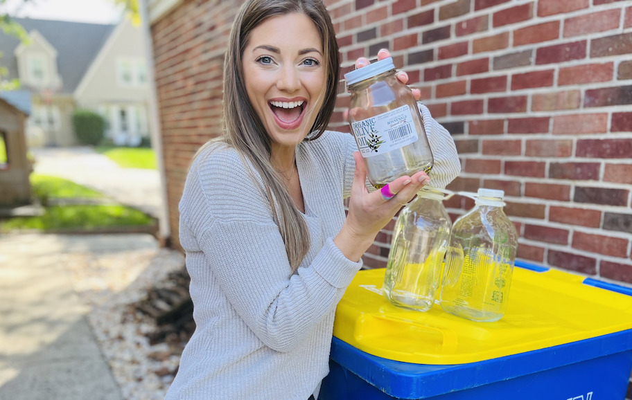 woman holding empty glass jar over recycling bin