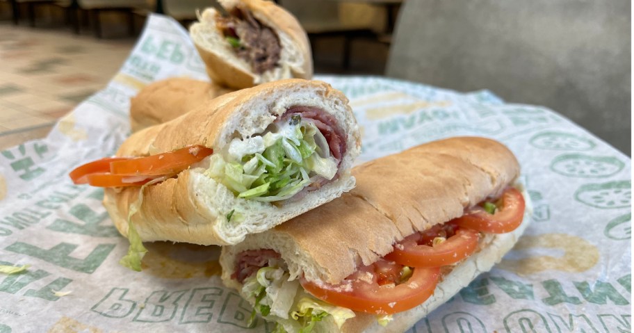 Two subway footlongs on table cut in half