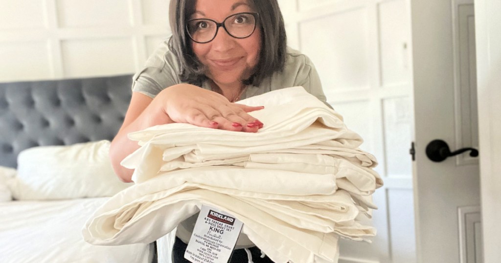 woman holding folded set of kirkland 680 Costco sheets