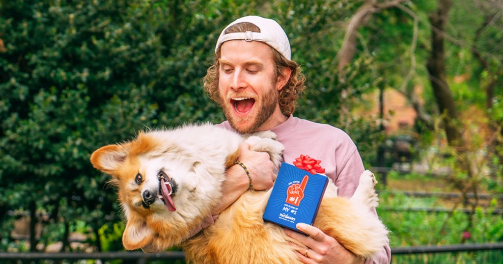 man holding corgi and box of poop bags