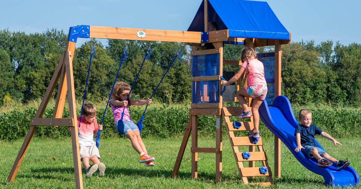 four kids playing on a Backyard Discovery Swing Set outside in front of trees