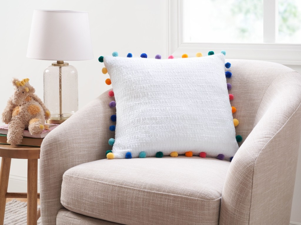 white pillow with colorful pom poms on chair