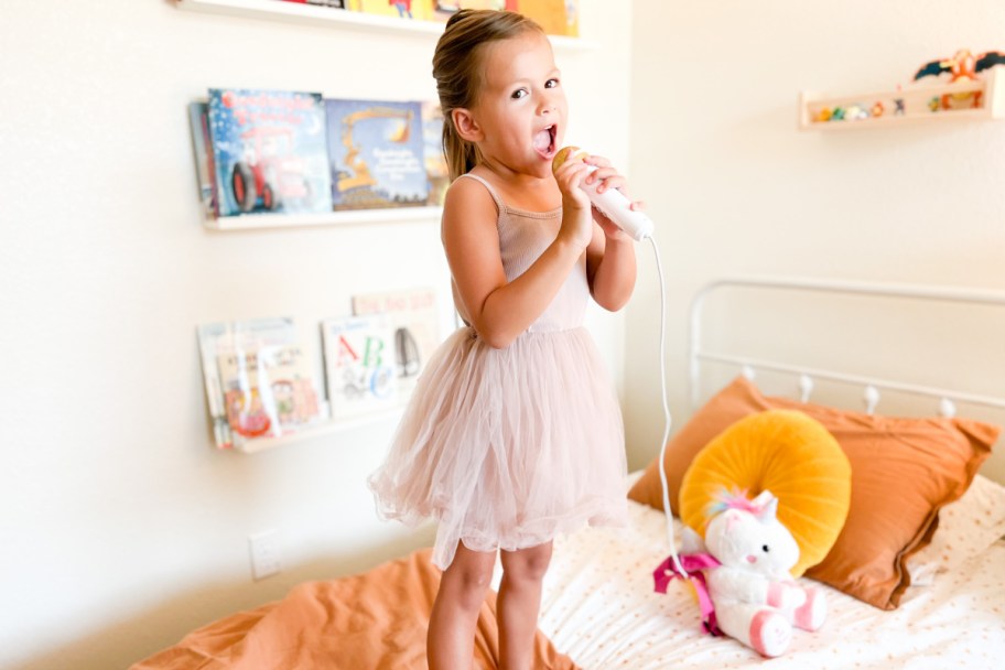 girl singing with sing along crew on bed in pink dress