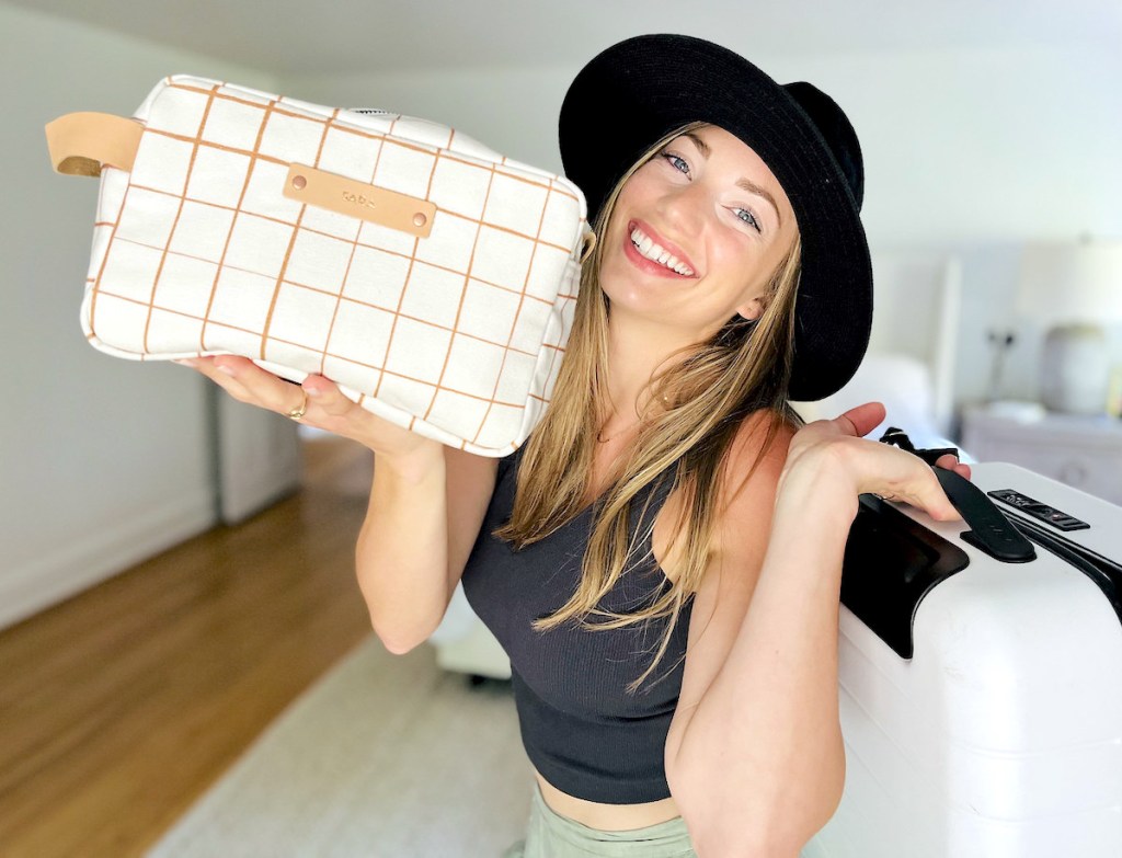 woman holding minted dopp kit toiletry bags and suitcase smiling