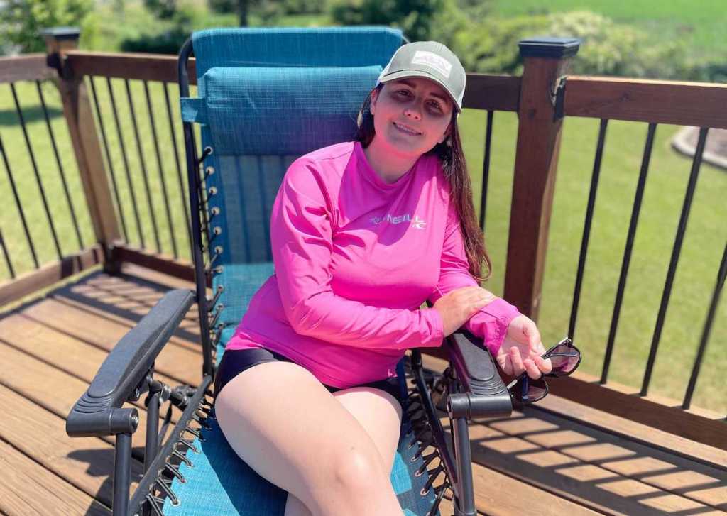 woman sitting in blue lawn chair wearing bright pink sun shirt