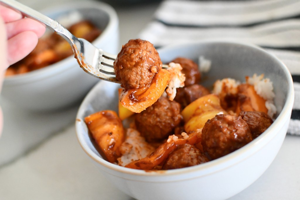 taking a bite of meatballs and bell peppers over rice