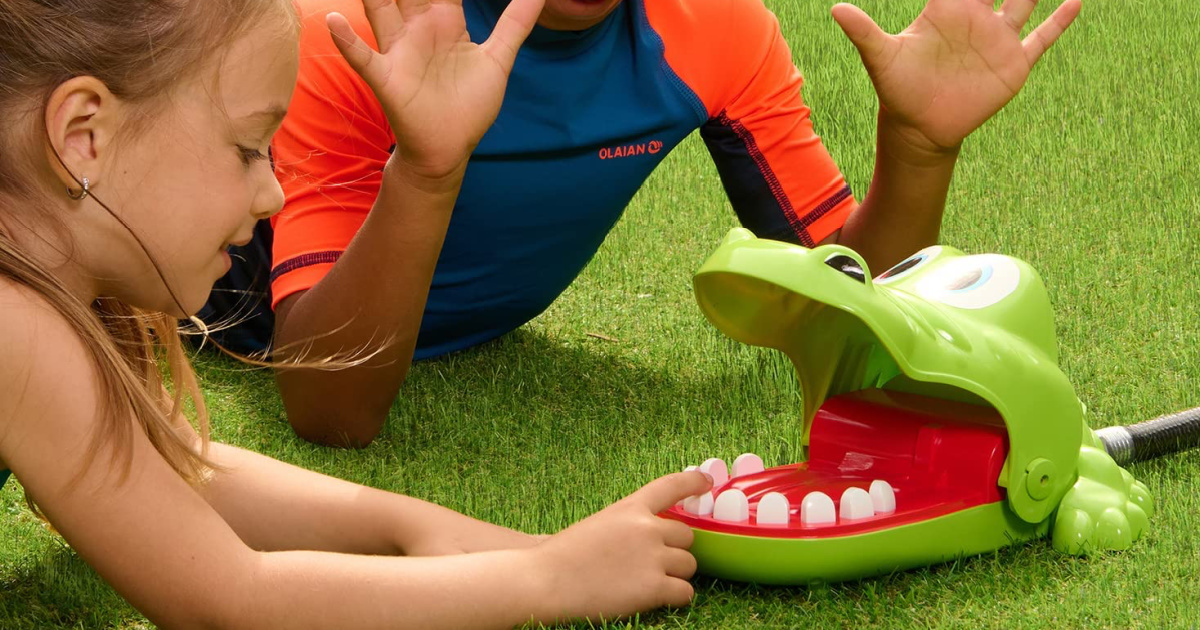 two kids laying on the grass, playing with the Hasbro Crocodile Dentist Splash Water Game attached to a hose