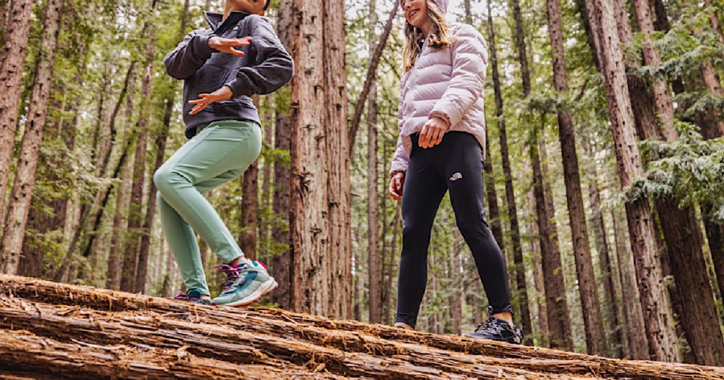 two girls walking on fallen tree in forest