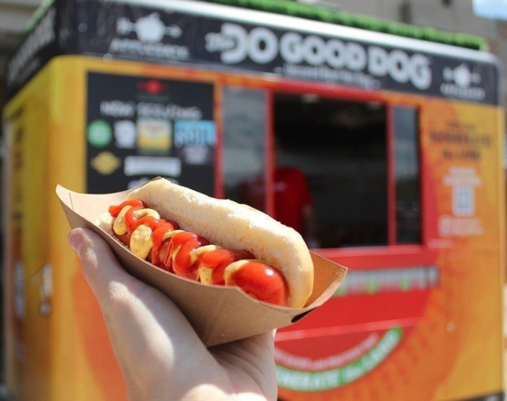 holding a hot dog in front of a hot dog cart