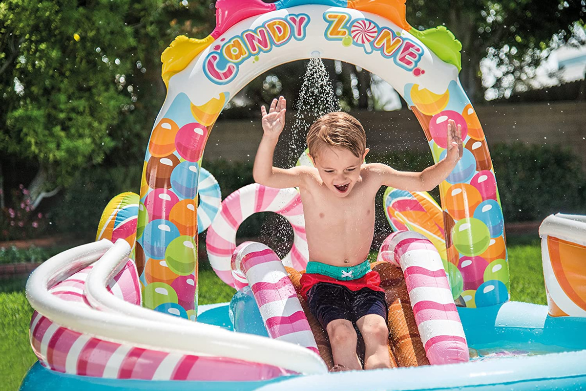 boy sliding down an inflatable intex candy zone play center while being sprayed with water