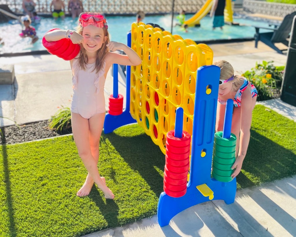 girl with connect 4 pieces on arms standing on turf with jumbo connect four board game for kids