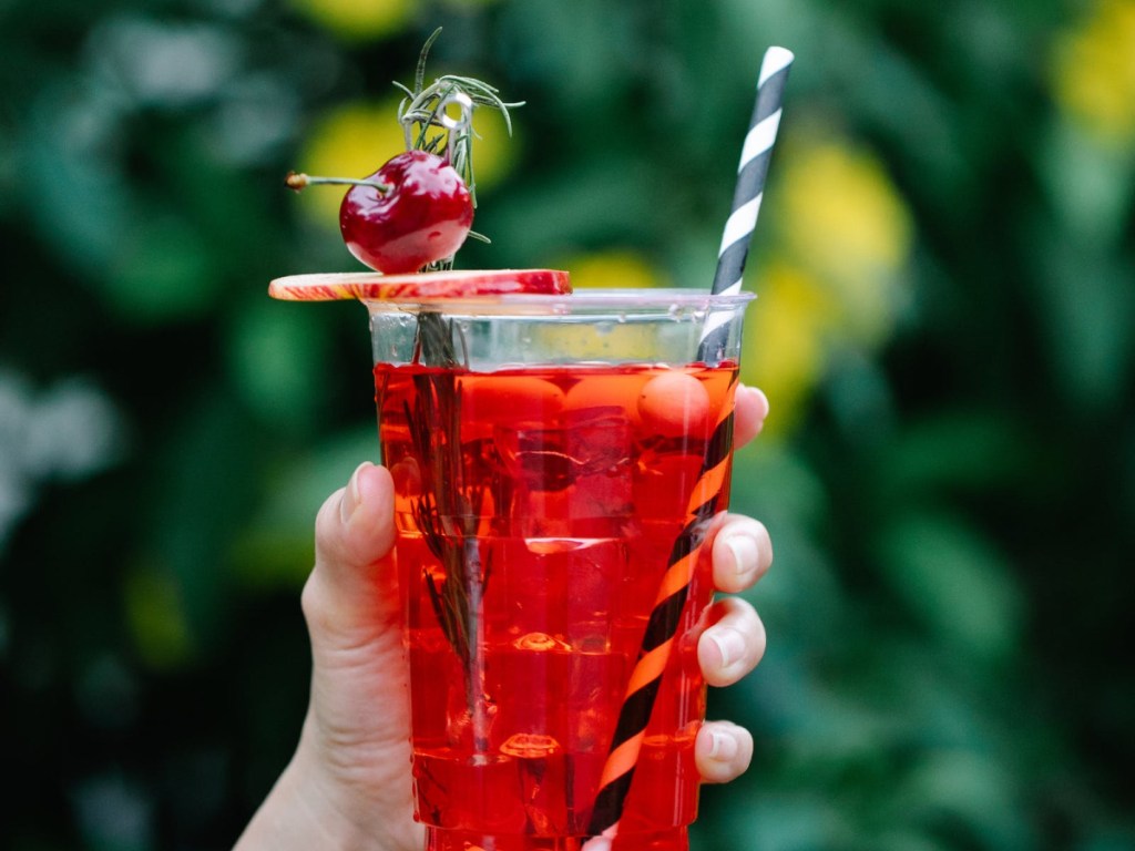 red beverage in a glass with a black and white straw topped with a cherry and apple slice