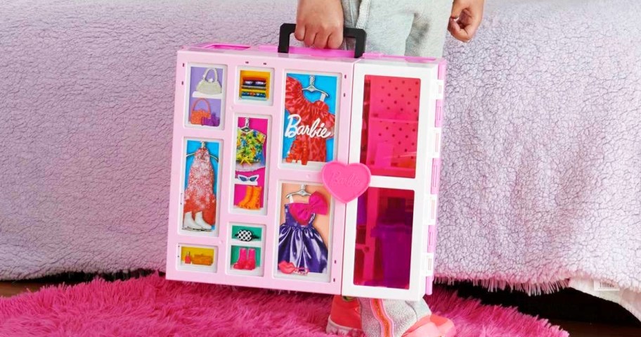 girl carrying a folded up Barbie Dream Closet playset