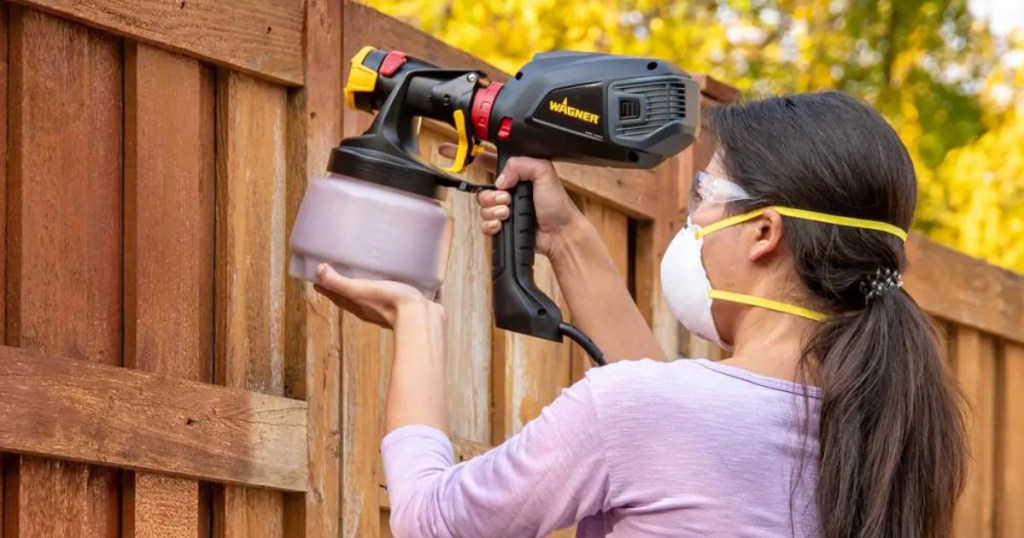 Woman using wagner paint sprayer on fence