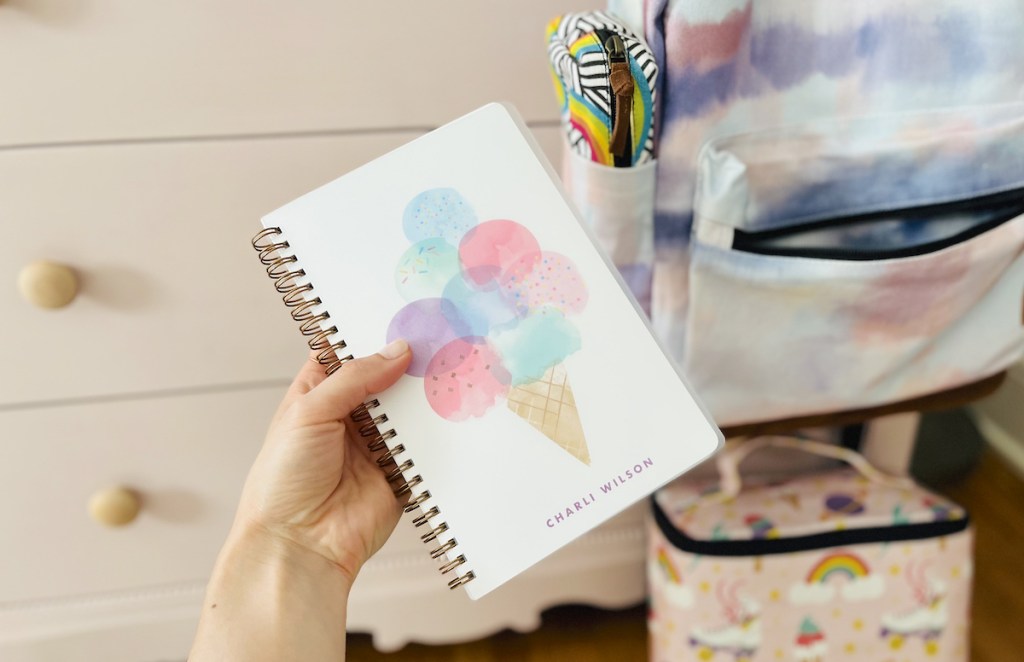 hand holding notebook in front of school supplies